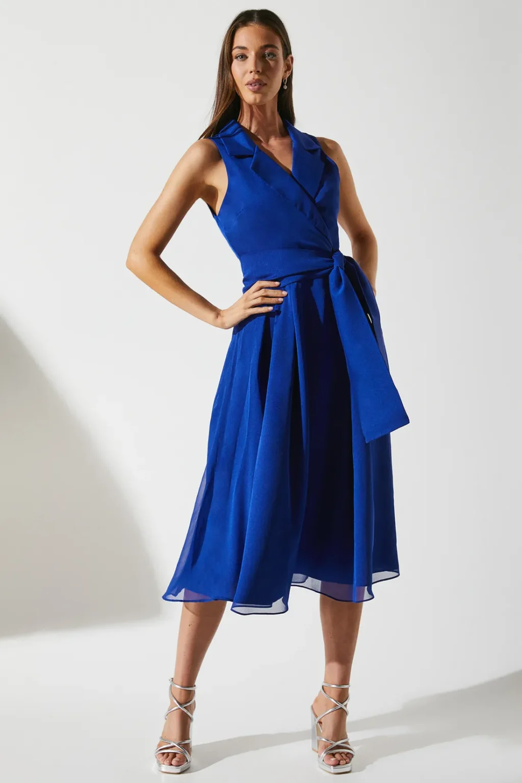 Woman wearing cobalt blue chiffon wrap dress with collar and waist tie, standing confidently in heels
