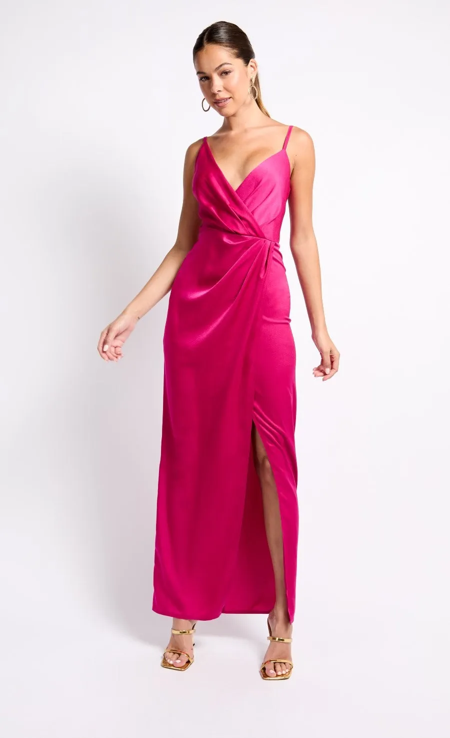 Woman in a hot pink satin wrap maxi dress with spaghetti straps and a thigh-high slit, standing confidently against a white background.