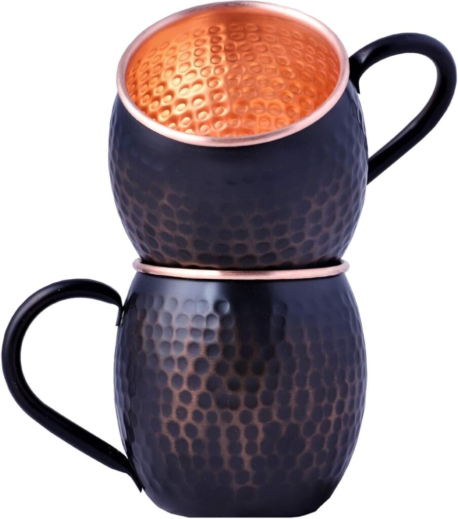 Set of two pure copper mugs with black hammered exterior and polished copper interior stacked on white background.