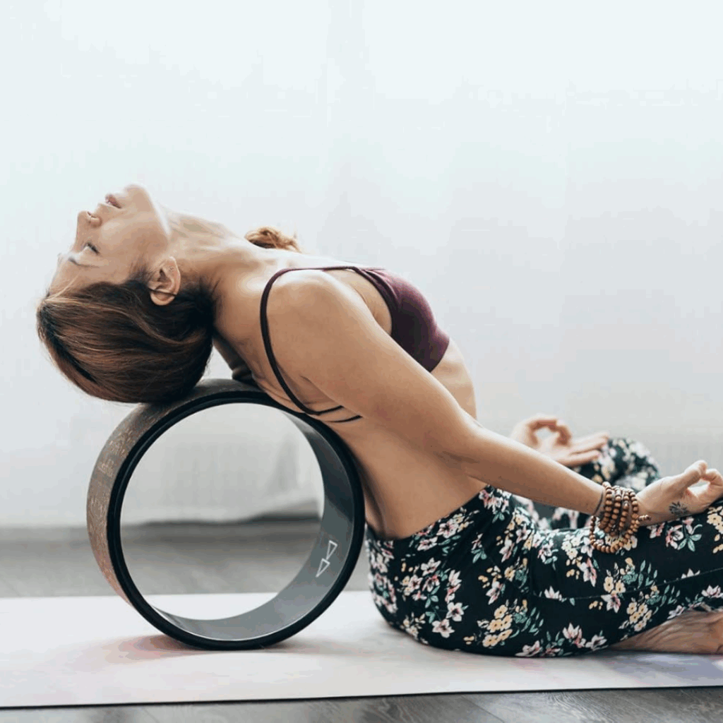 Woman leaning back onto a yoga wheel with hands resting by her sides, using the tool for spinal release and posture support