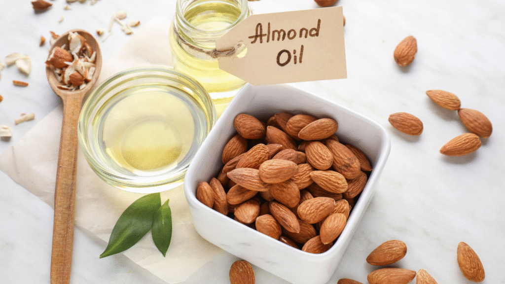 Almond oil in glass jars with raw almonds in a bowl and spoon on a marble surface.