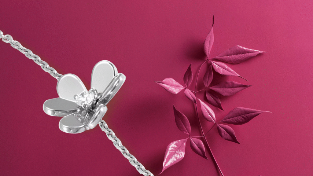 Van Cleef & Arpels Frivole white gold bracelet with diamond flower on magenta background beside metallic pink leaves.