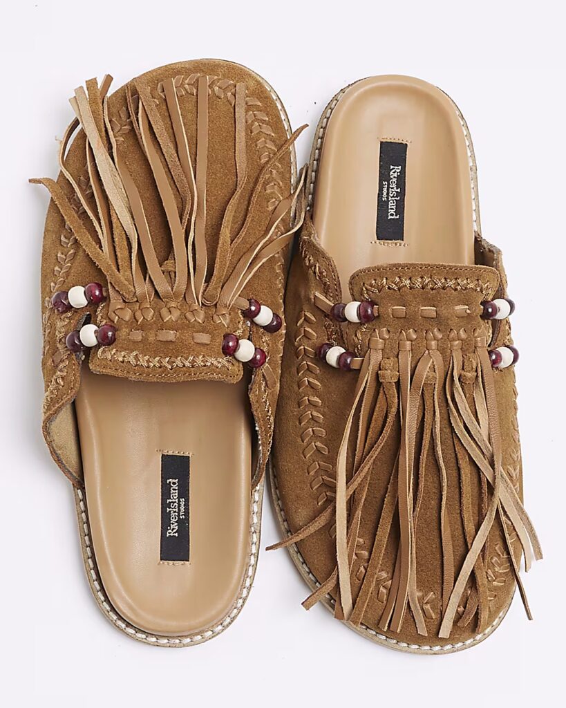 Tan suede clogs with fringe detailing and beaded embellishments, viewed from above on a white background.