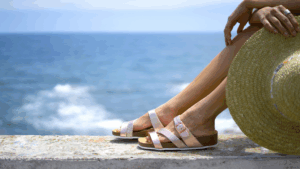 women’s feet wearing strappy summer sandals, photographed against a blue ocean backdrop.